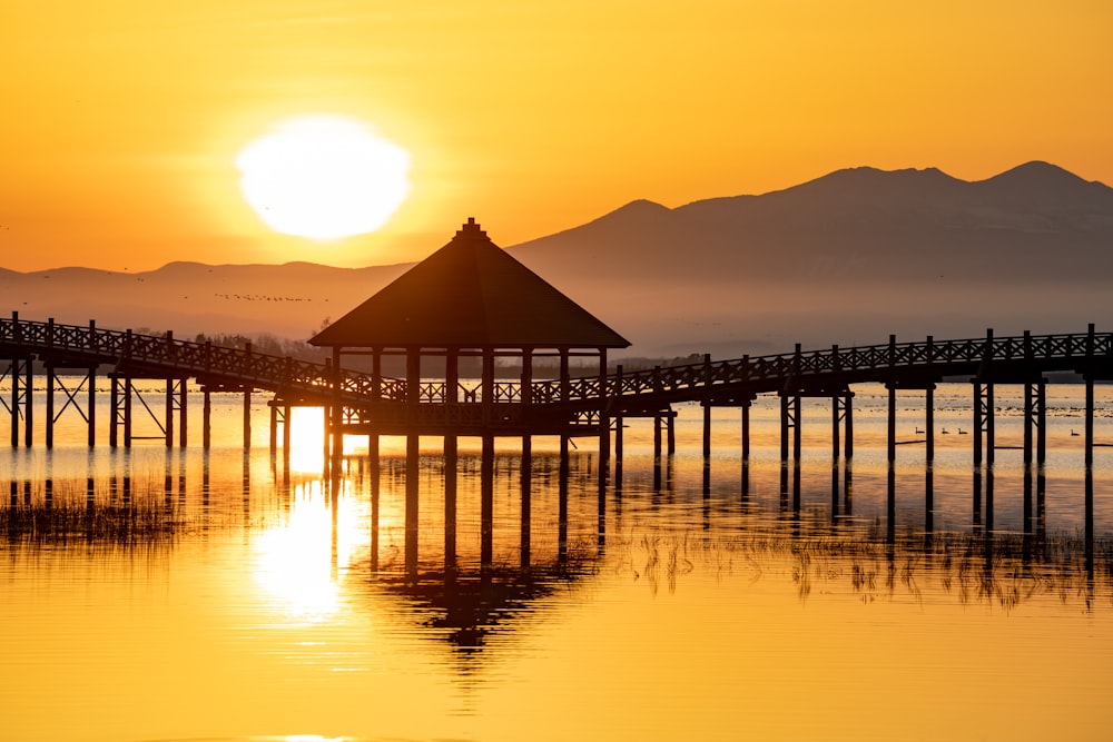 the sun is setting over the water with a pier in the foreground