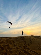 a person standing on top of a sandy hill flying a kite
