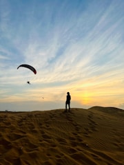 a person standing on top of a sandy hill flying a kite