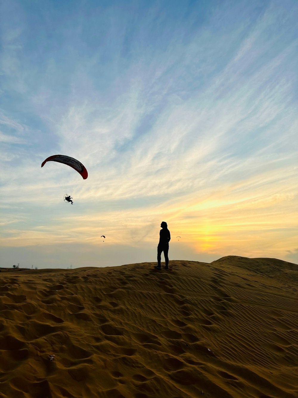 a person standing on top of a sandy hill flying a kite