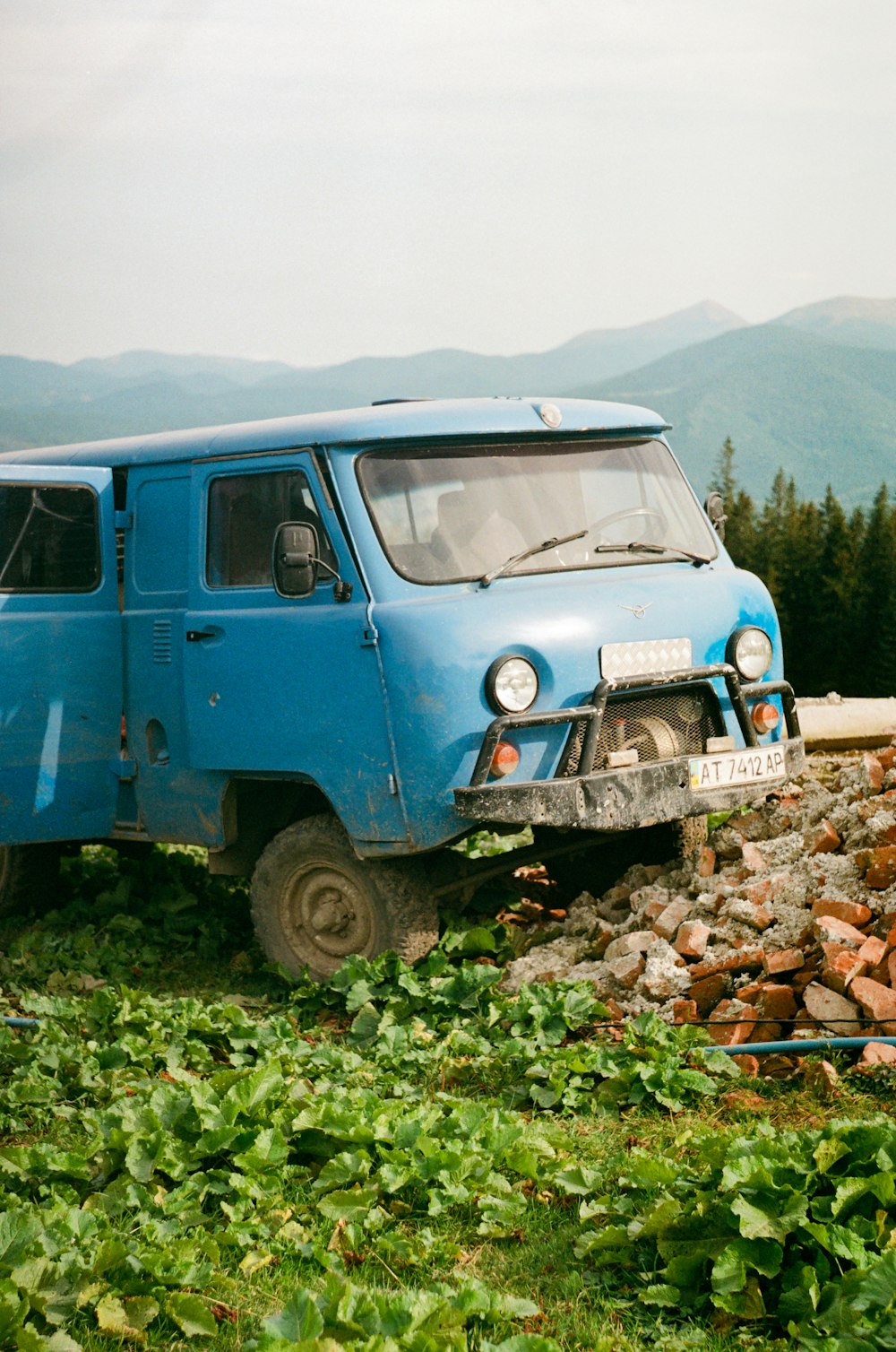 a blue van parked on top of a lush green hillside