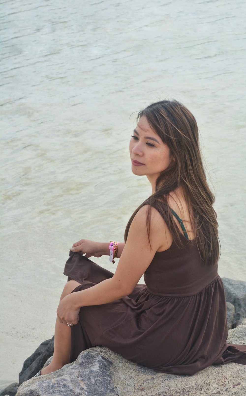 a woman sitting on a rock by the water