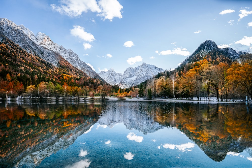 a lake surrounded by mountains and trees in the fall