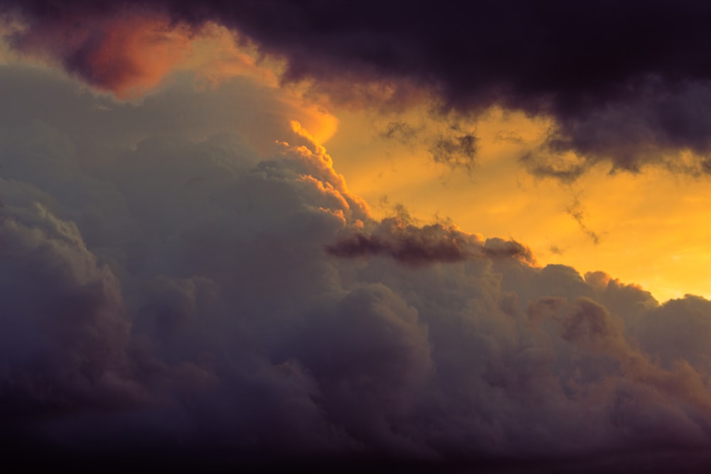 a plane flying through a cloudy sky at sunset