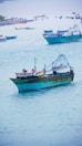 Several fishing boats are anchored in a calm sea, with one large blue and yellow boat prominently in the foreground. Smaller boats are scattered in the background against a soft horizon. The scene suggests a quiet day in a coastal fishing area.