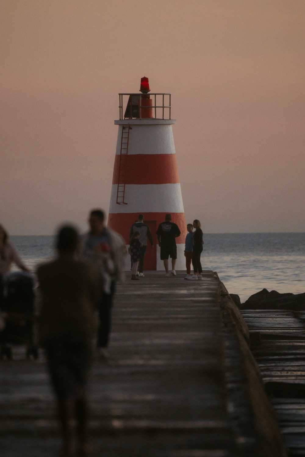a group of people standing on a pier next to a light house