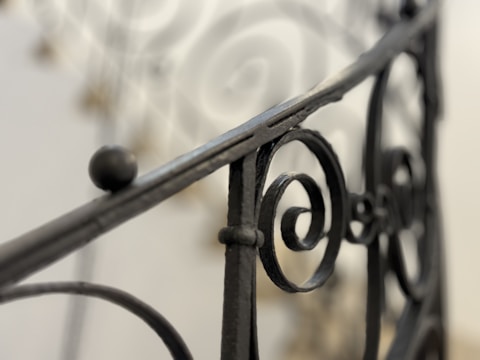 Ornate black wrought iron railing with intricate spiral patterns set against a softly blurred background.