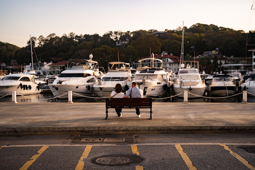 a couple sitting on a bench in front of a marina