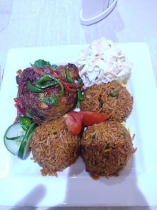 A steaming plate of tender chicken served over fragrant rice with a side of fresh cucumber slices.