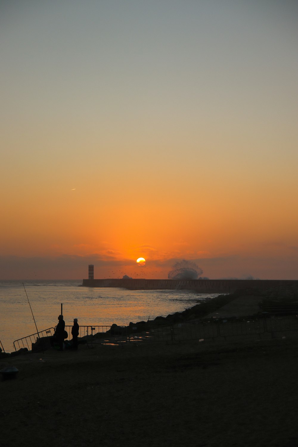 a couple of people sitting on a beach watching the sun set