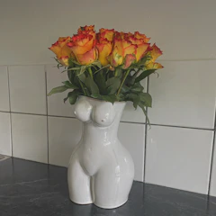 A close-up of a textured ceramic vase in cheerful orange and green hues, holding fresh wildflowers.