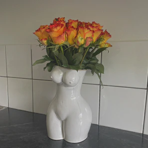 A close-up of a textured ceramic vase in cheerful orange and green hues, holding fresh wildflowers.