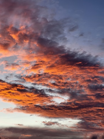 Vibrant and dynamic clouds with shades of orange and pink against a deep blue sky, creating a striking contrast. The cloud formations appear layered and textured, adding depth to the scene.