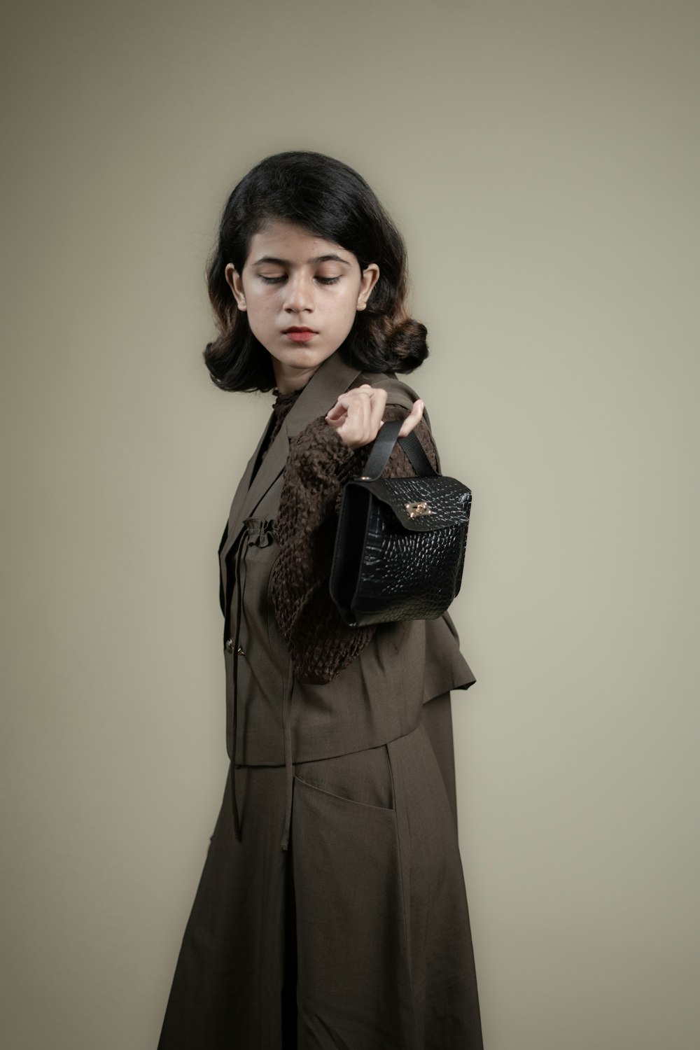 a woman in a brown coat holding a black purse