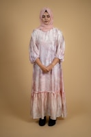 A South Asian woman in a soft pink flowing dress, standing gracefully against a white backdrop.