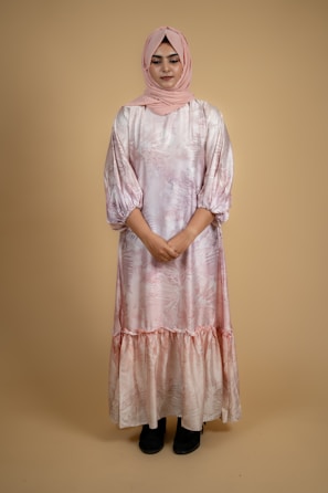 A South Asian woman in a soft pink flowing dress, standing gracefully against a white backdrop.