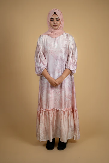 Model wearing a flowing dusty rose dress standing against a soft cream background.