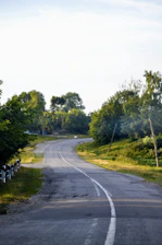 A peaceful rural mountain road winding through lush greenery under a clear sky.