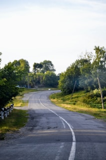 A freshly paved rural road winding through green hills under a clear blue sky.