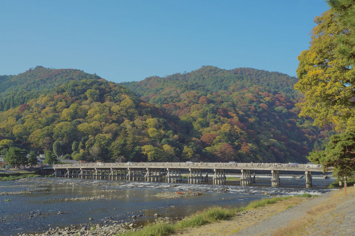 A wooden bridge spanning a river with forested mountains rising in the background at Arashiyama