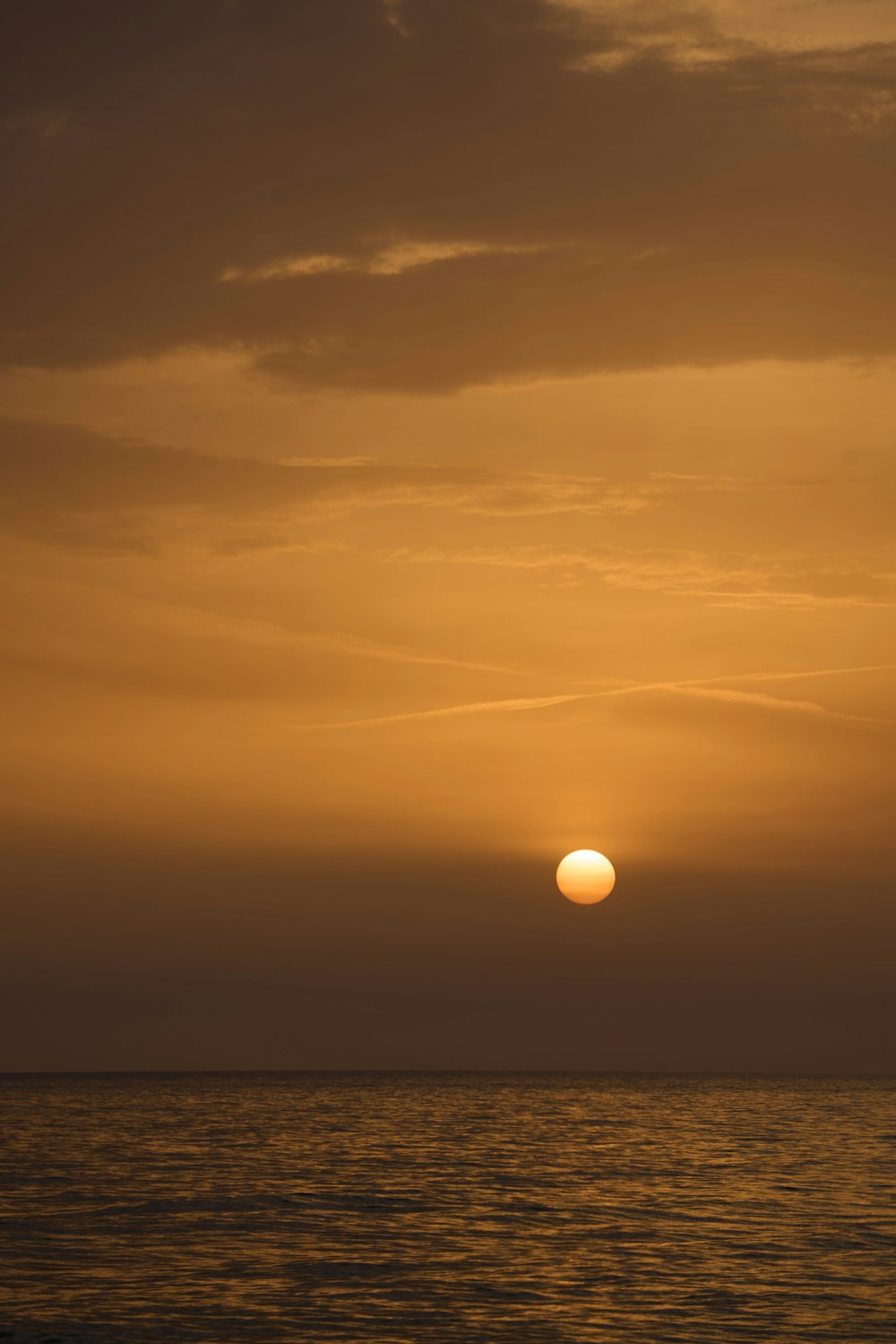 the sun is setting over the ocean on a cloudy day