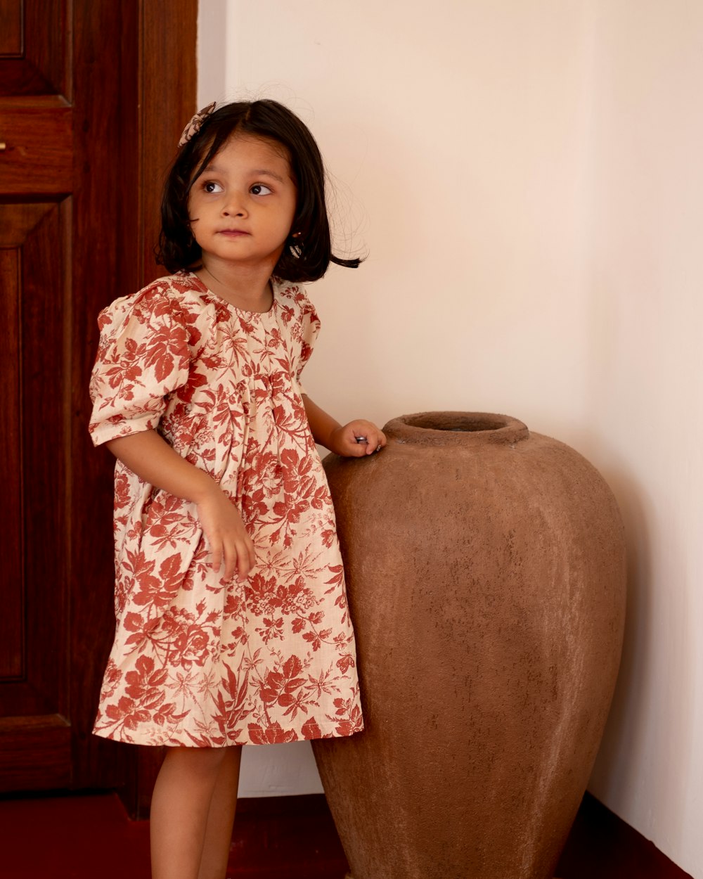 a little girl standing next to a large vase