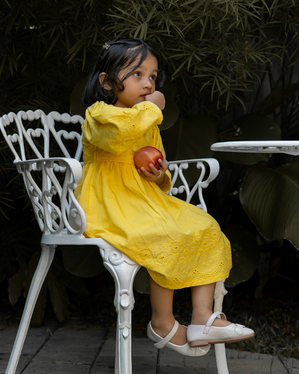 a little girl in a yellow dress sitting on a white chair