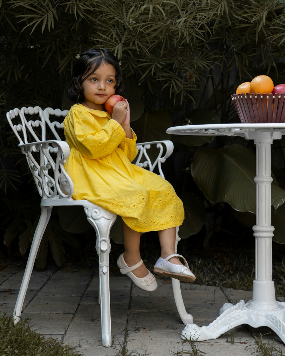 a little girl sitting at a table eating an apple