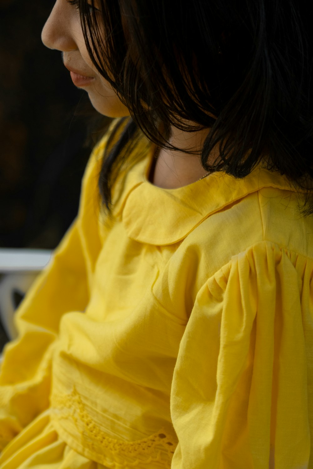 a little girl in a yellow dress sitting on a bench