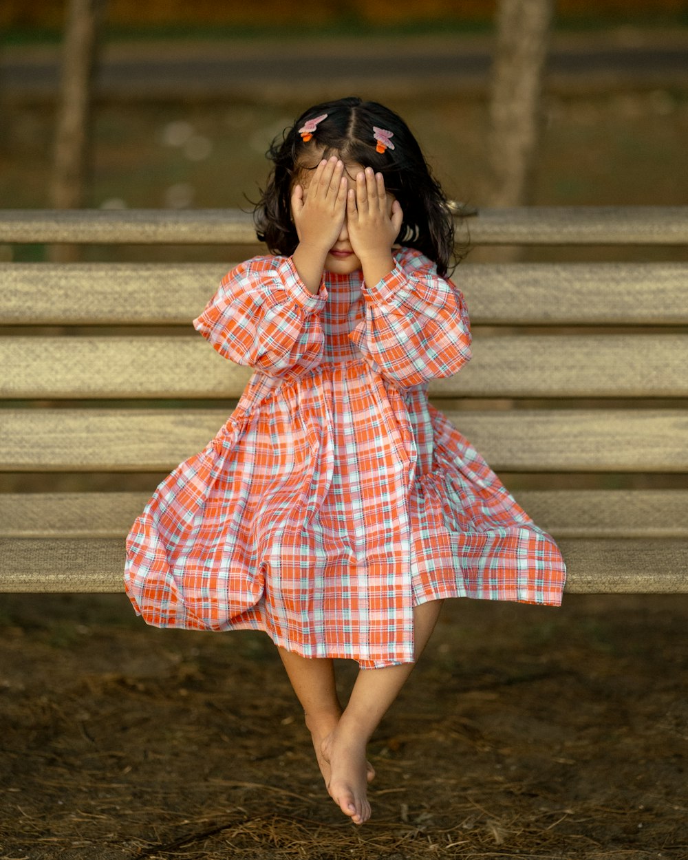 a little girl covering her face while sitting on a bench