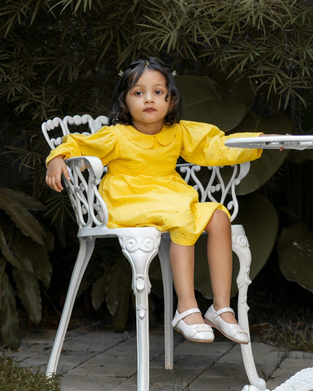 a little girl in a yellow dress sitting on a white chair