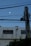 A pale moon is visible in a clear, evening sky above a building. The building's facade displays several names and text, possibly listings or commemorations. In the foreground, a utility pole with cables extends diagonally across the scene.