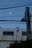 A pale moon is visible in a clear, evening sky above a building. The building's facade displays several names and text, possibly listings or commemorations. In the foreground, a utility pole with cables extends diagonally across the scene.