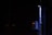 A dimly lit scene featuring a vertical pipe and an electrical panel with glowing indicator lights. The surrounding environment is mostly dark, highlighting the contrast with the illuminated objects.