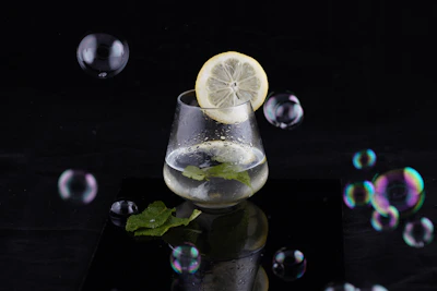 Close-up of a woman’s hands holding a glass of infused water with fresh herbs and lemon slices.