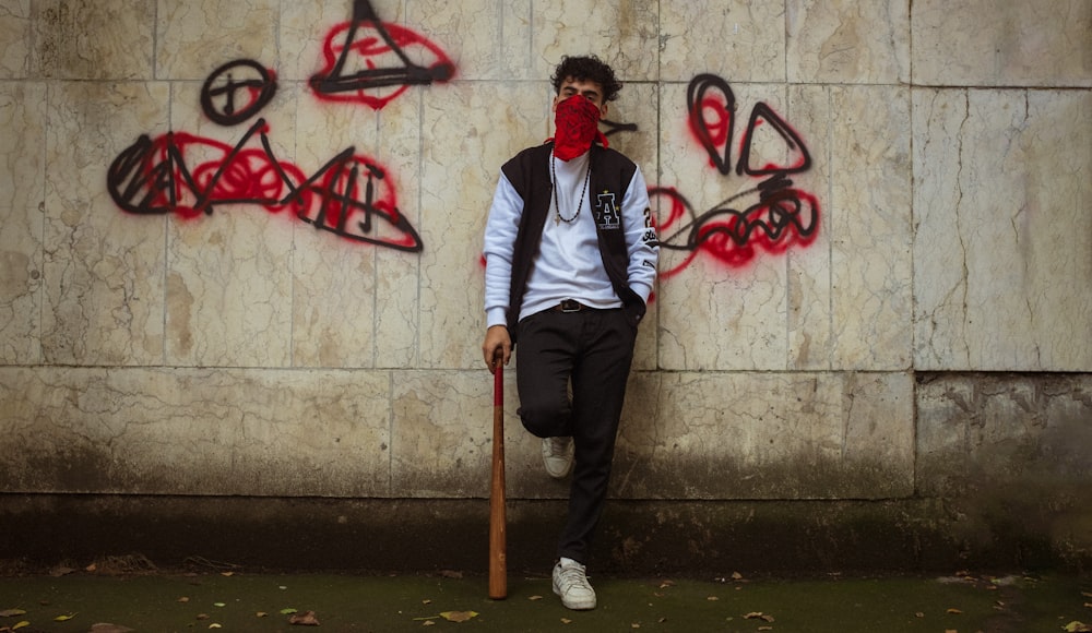 a man with a baseball bat leaning against a wall covered in graffiti