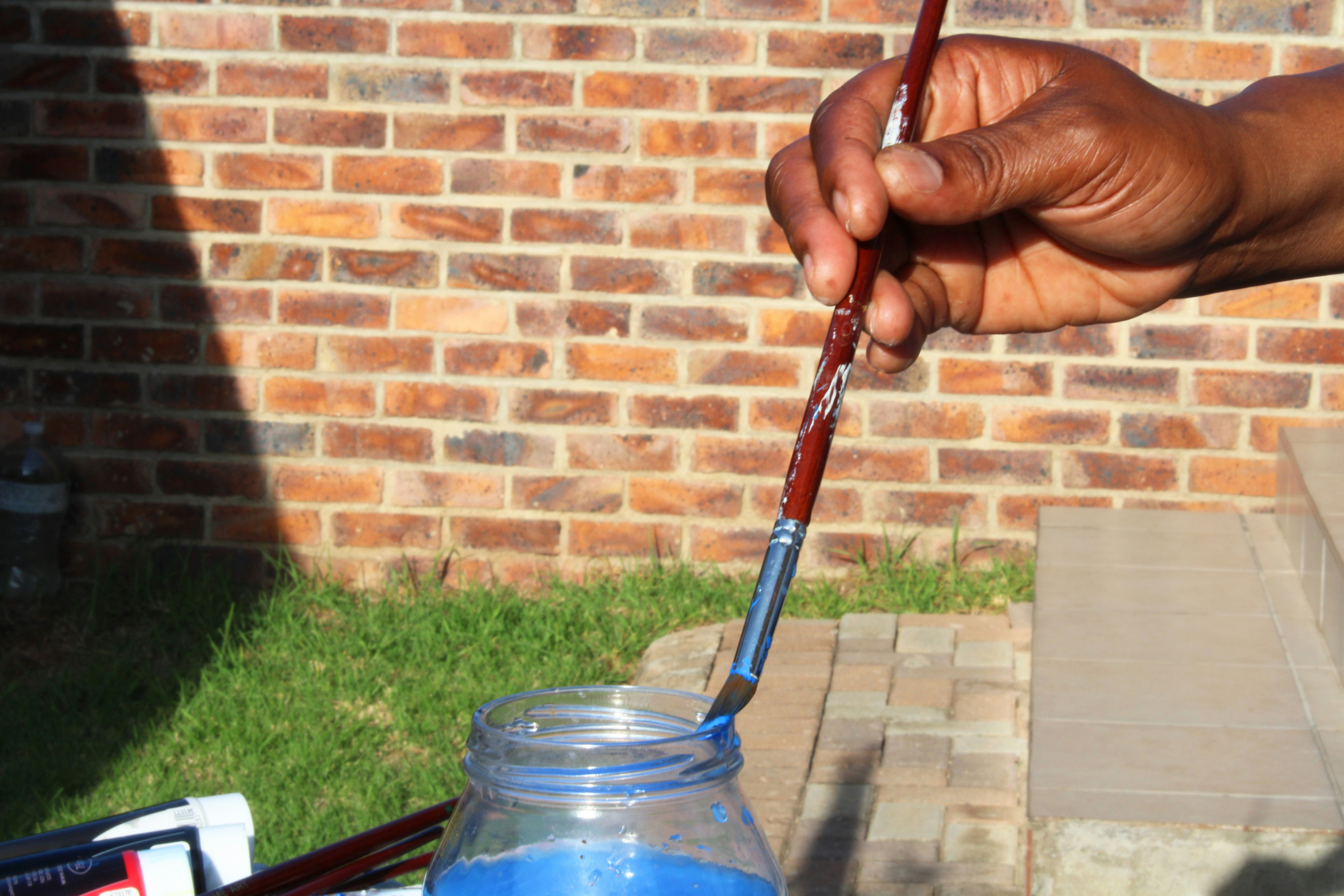 a person holding a paintbrush over a jar of blue liquid