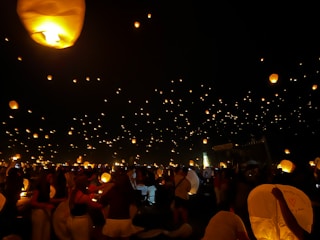 Nighttime view of the festival with glowing lanterns floating above the crowd.