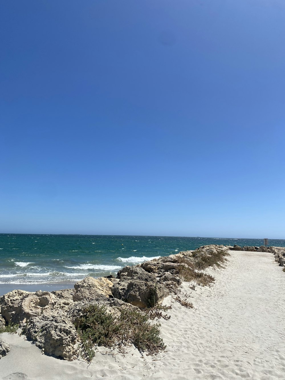 a sandy beach next to the ocean under a blue sky