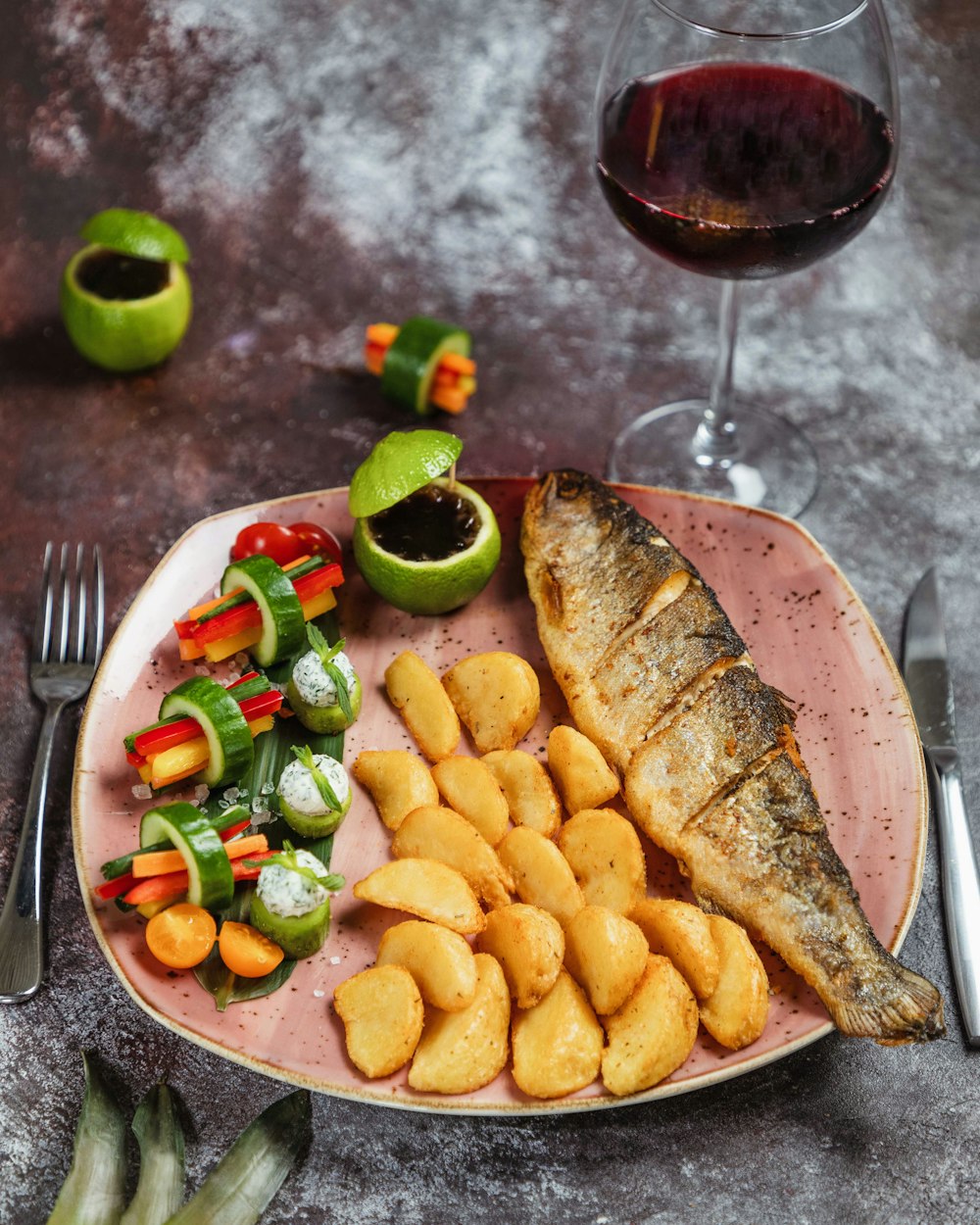 un plato de pescado, patatas y verduras con una copa de vino