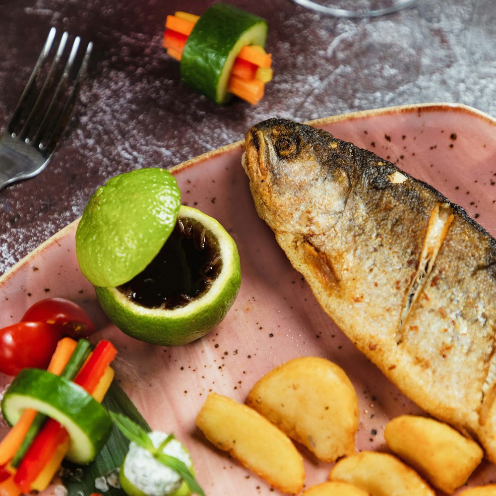 un plato rosado cubierto con pescado junto a un montón de gajos de patata