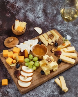 a wooden cutting board topped with cheese and grapes