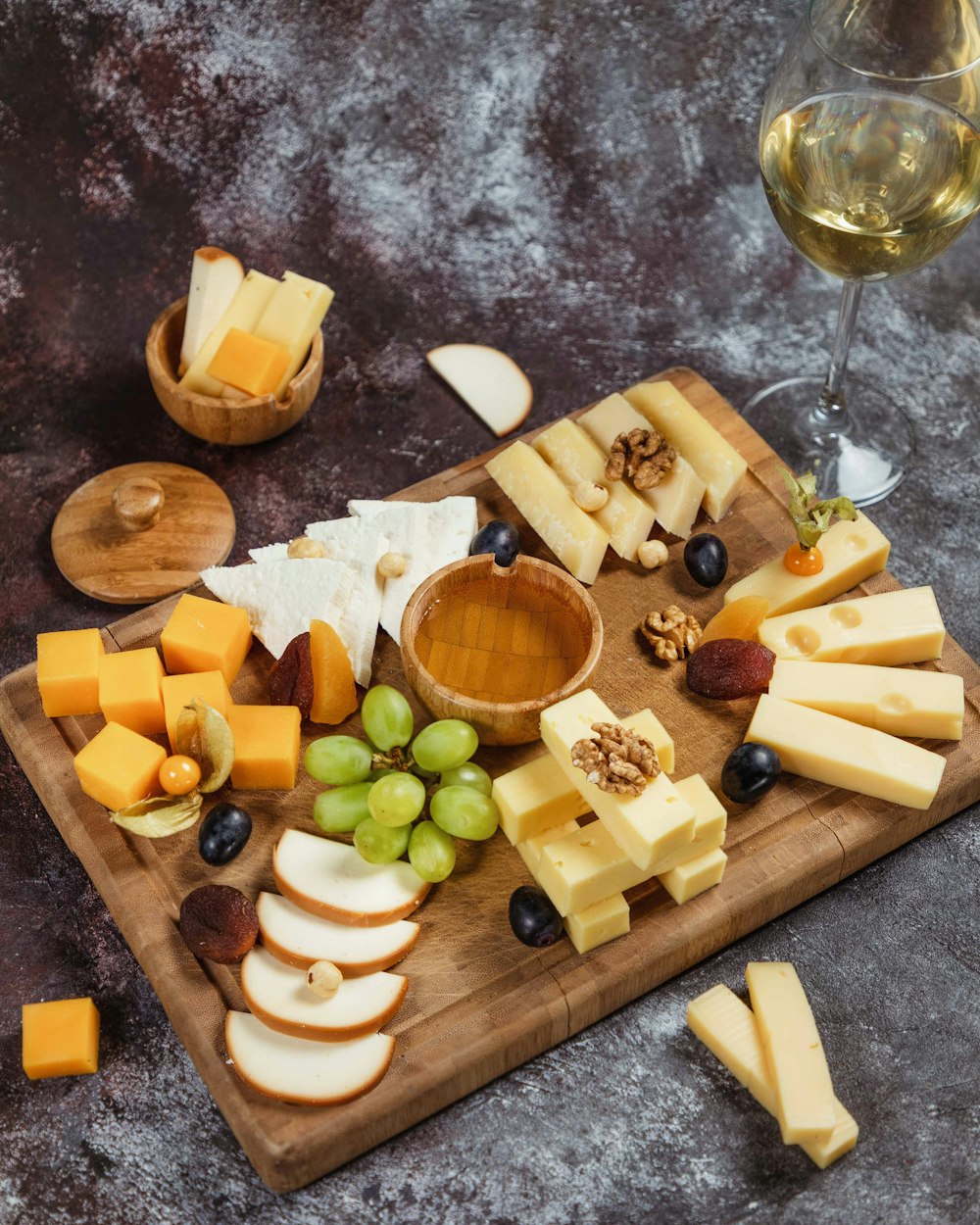 a wooden cutting board topped with cheese and grapes