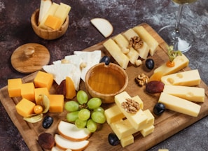 a wooden cutting board topped with cheese and grapes