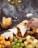 A hand dips a triangular piece of white cheese into a bowl of honey surrounded by various types of cheese, nuts, dried fruits, and grapes. A glass of white wine is visible in the background.