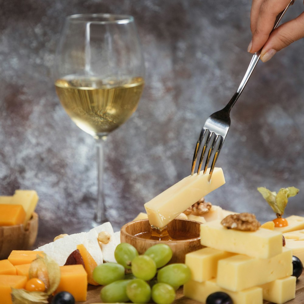 a person holding a fork over a plate of cheese and grapes