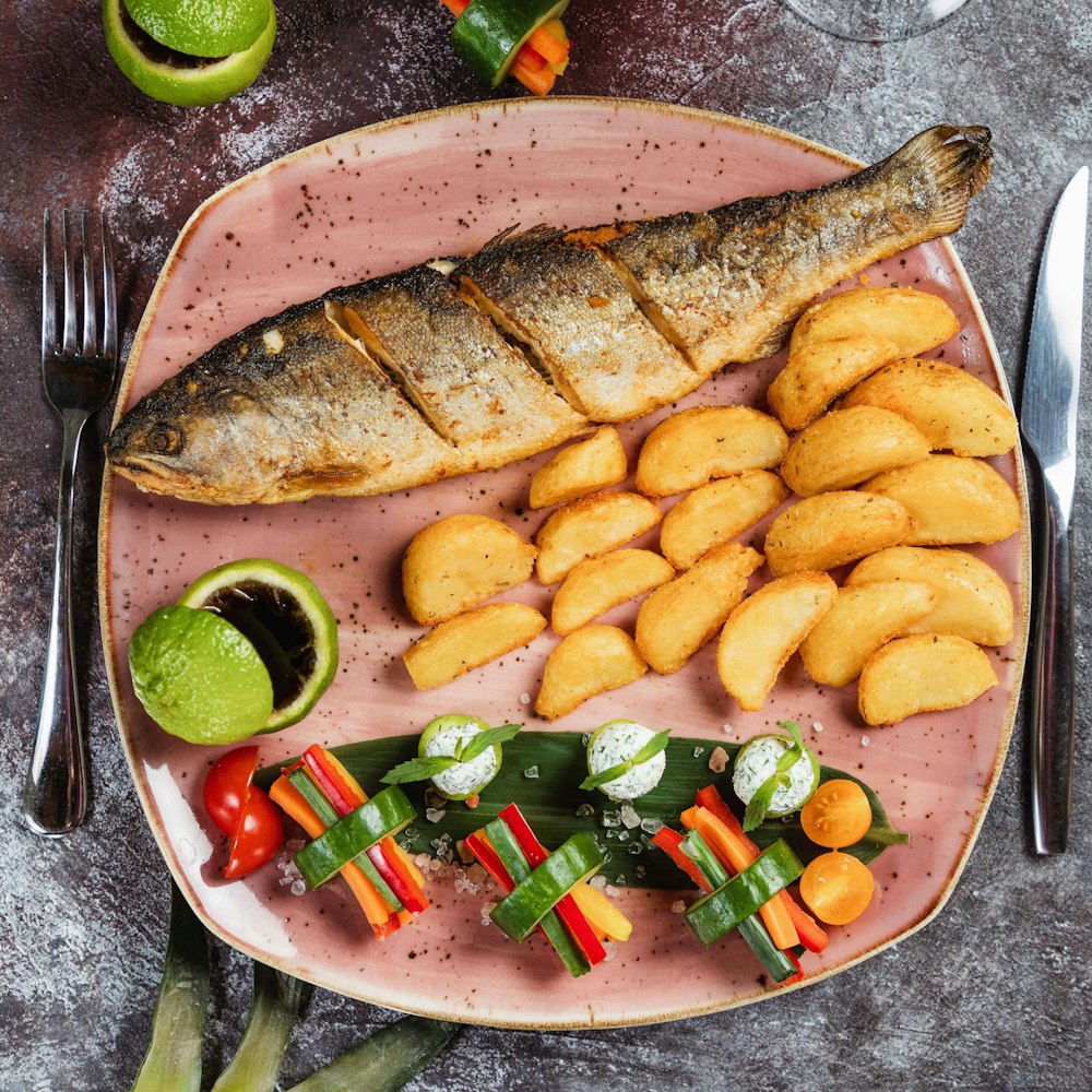 a pink plate topped with fish and veggies