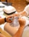 A nail salon setting featuring two hands, one receiving a manicure while the other is filing the nails. The workspace includes a ventilation device and a selection of colored nail polish samples.