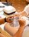 A nail salon setting featuring two hands, one receiving a manicure while the other is filing the nails. The workspace includes a ventilation device and a selection of colored nail polish samples.