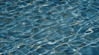 Close-up of water dripping from a hidden crack beneath pool tiles.